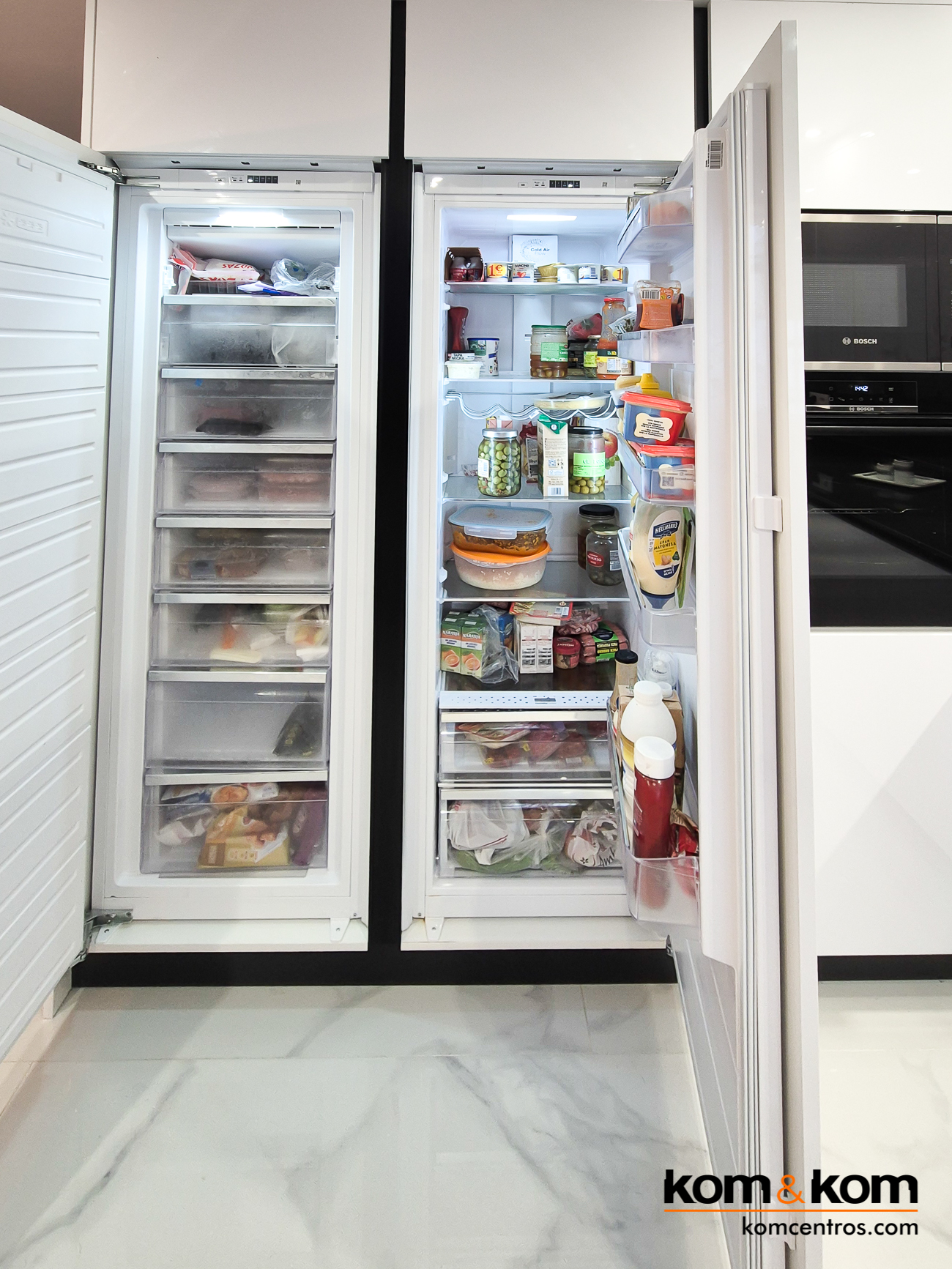 Columnas con frigorífico y congelador integrados en cocina moderna de mármol negro y blanco brillo. Las puertas están abiertas, por lo que se ve el interior del refrigerador y el congelador. Ambos están llenos de comida.